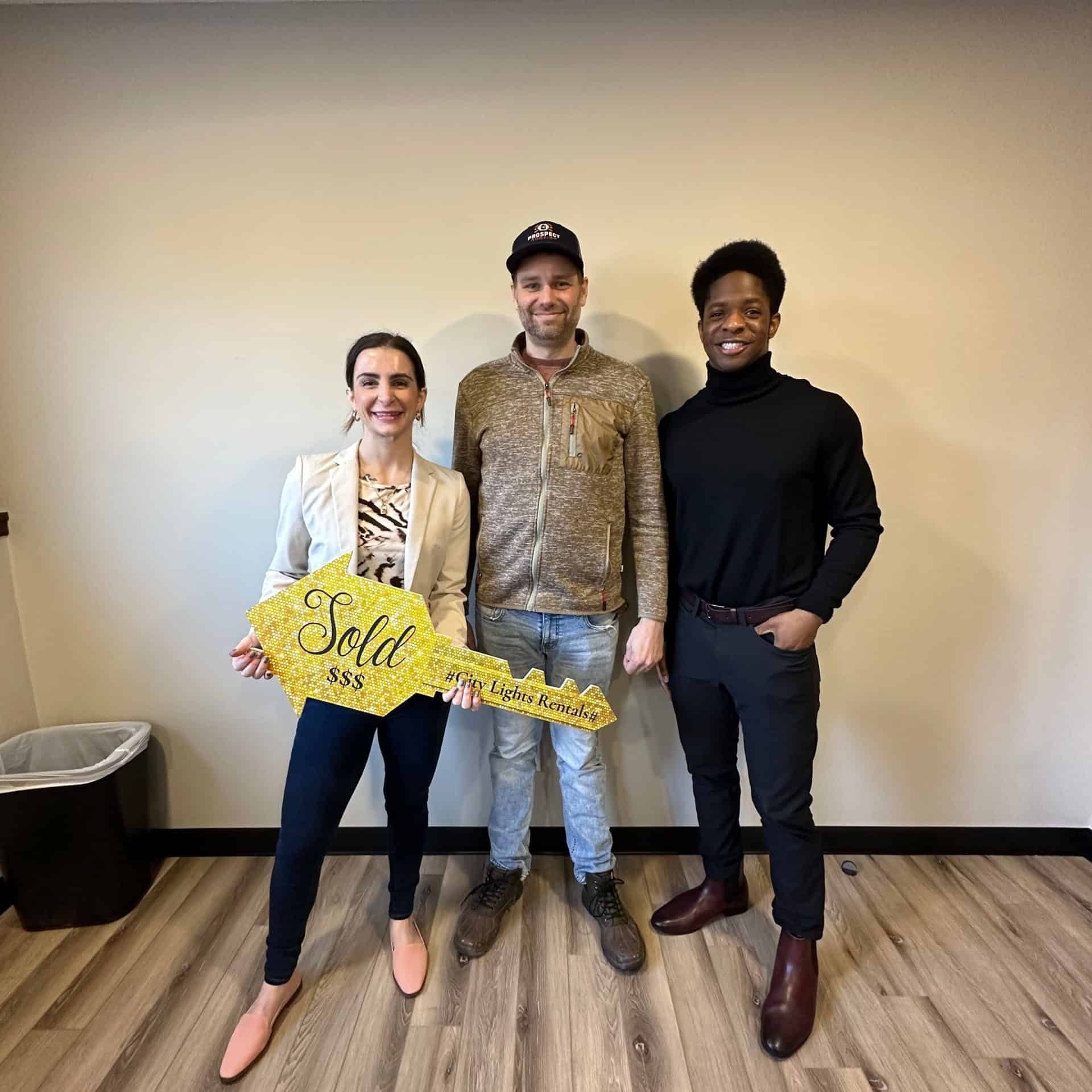 Ryann Brier and Caleb Reits posing with a home seller and a Sold sign