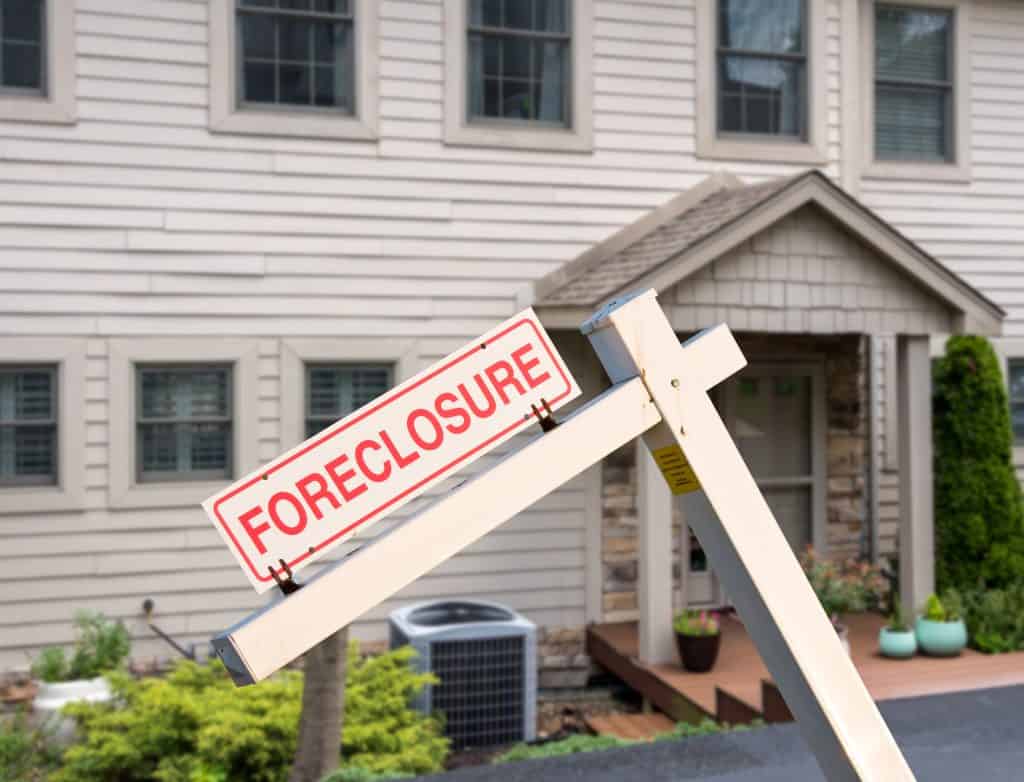 Foreclosure sign in front of a house indicating a property in distress.